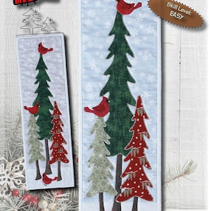 May include: A fabric wall hanging with the text "Cardinals in Winter Trees" and dimensions of 6.5" x 21". The design features red cardinals perched on green and red trees against a light blue snowy background. The skill level is "EASY".