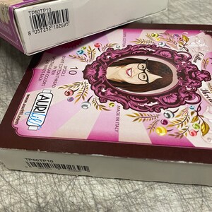 May include: A box of 70 spools of 50 weight cotton thread in ten spectacular colors. Each spool contains 220 yards of thread. The box is brown with a pink and white design featuring a woman with glasses. The text "Aurifil" is written in blue on the box. The box has a barcode with the product code TP50TP10.