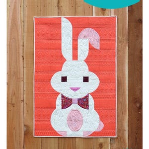 May include: A white bunny with a pink bow tie on a coral background with a diamond pattern. The bunny is a quilt pattern titled "Posh Bunny" from Sew Kind of Wonderful. The pattern number is #449.