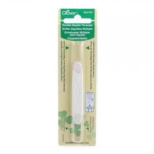 May include: White plastic double needle threader for sewing machines. The packaging has green clover leaves and the text "Double Needle Threader", "Enfile-Aiguilles Multiple", "Enhebrador Múltiple para Agujas", "Doppelinfädler", "Large Needles/Sewing Machine Needles", "Grandes Aiguilles/Aiguilles pour Machine à Coudre", "Agujas Grandes/Agujas para Máquinas de Coser", "Große Nadeln/Nähmaschinennadeln", "Small Needles", "Petites Aiguilles", "Agujas Pequeñas", "Kleine Nadein", "Clover 462/NV" and "CLOVER mfg. CO., LTD."