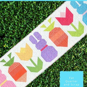 May include: A table runner with a bunny, tulips, and carrots in a patchwork design. The runner is 22 inches by 70 inches and is made with fat quarters and scraps. The text "Bunny Trail Table Runner" is at the top of the image.