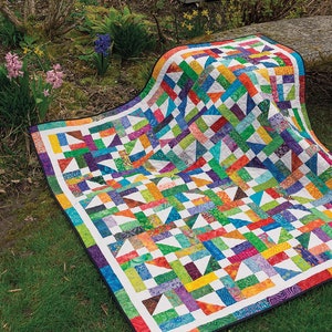 May include: A colourful patchwork quilt with a geometric pattern in shades of green, blue, orange, purple, and white. The quilt is made of various fabrics and is laid out on a grassy lawn.