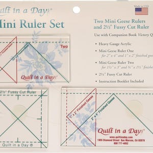 May include: Quilt in a Day Mini Ruler Set includes two acrylic mini geese rulers and a 2 1/2 inch fussy cut ruler. The rulers are clear and have green lines. The set is packaged in a clear plastic bag with a white card backing. The card backing has the Quilt in a Day logo and website information.