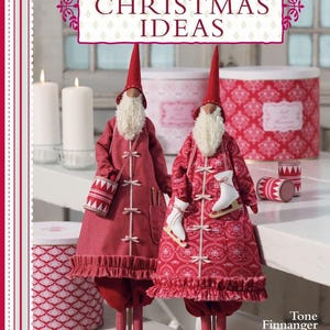May include: Two red and white Christmas gnomes with white beards and hats. The gnome on the left is holding a red and white bucket. The gnome on the right is holding a white ice skate. The gnomes are standing on a white surface. The text "Tilda's Christmas Ideas" is at the top of the image. The text "Tone Finnager" is at the bottom of the image.