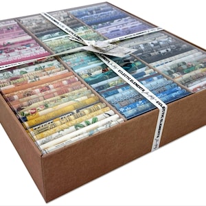 May include: A brown cardboard box filled with fabric rolls in various colors, including pink, blue, yellow, and green. The rolls are arranged in compartments under a clear plastic lid. A white ribbon with the text "Eclectic Elements" wraps around the box.
