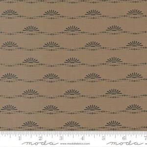 May include: A brown fabric with a repeating pattern of black stylized suns and dots. The fabric is measured with a ruler in inches. The ruler has the word "moda" printed on it.
