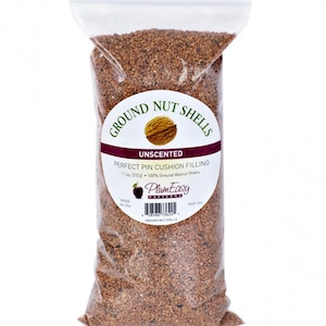 May include: A clear plastic bag filled with brown ground nut shells. The label reads GROUND NUT SHELLS, UNSCENTED, PERFECT PIN CUSHION FILLING, 11 oz. (312 g), 100% Ground Walnut Shells, PlumEasy PATTERNS, MADE IN USA, and includes a barcode.