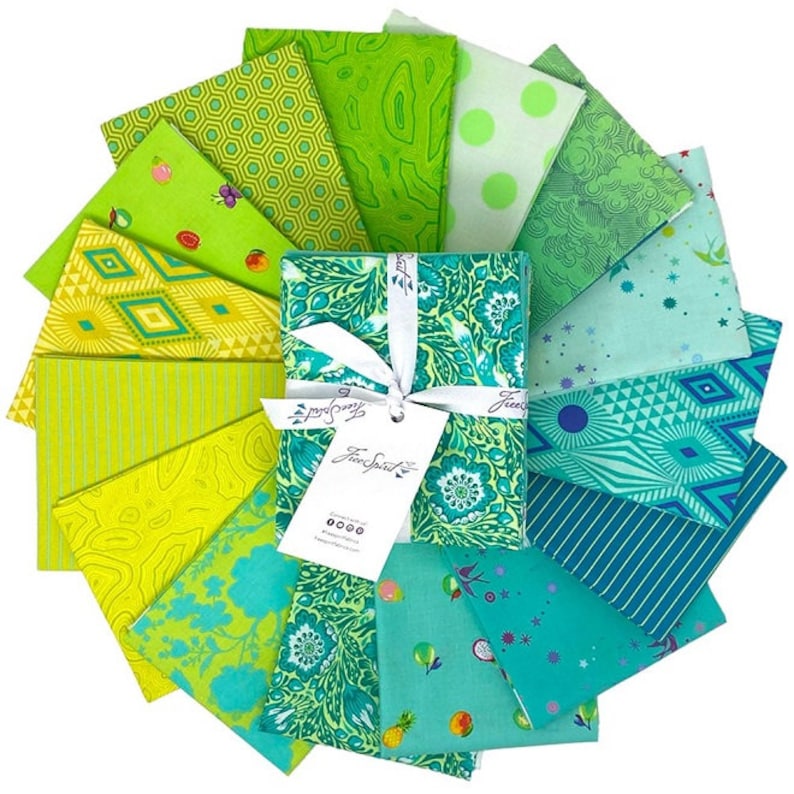 Op de afbeelding: Een set van 15 stoffen vierkanten in verschillende tinten groen, blauw en geel. De stoffen vierkanten zijn in een waaier vorm gerangschikt en hebben verschillende patronen, waaronder geometrische ontwerpen, bloemenprints en abstracte patronen. De stoffen vierkanten zijn samen verpakt met een wit lint en een label met de tekst "Free Spirit".
