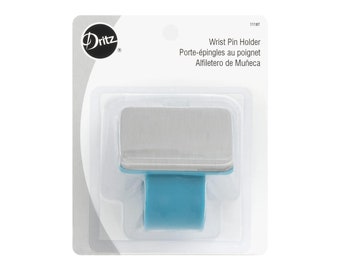 May include: A Dritz brand wrist pin holder in retail packaging. The device features a rectangular, brushed silver-tone metal top plate attached to a solid, bright blue flexible band. The packaging includes the text Wrist Pin Holder.