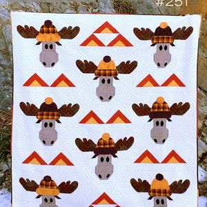 May include: A quilt pattern featuring a moose wearing a plaid hat. The pattern is called "Chocolate Moose #251" and is from Cotton Street Commons.