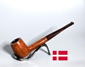 May include: A wooden tobacco pipe with a curved bowl and a long, slender stem. The bowl has a light brown, patterned finish, while the stem is a dark brown. The pipe rests on a silver-colored stand. A Danish flag is in the background.