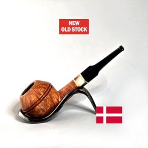 May include: A wooden tobacco pipe with a curved stem and a black mouthpiece. The pipe is displayed on a metal stand. The text "NEW OLD STOCK" is in a red rectangle. A Danish flag is in the image.