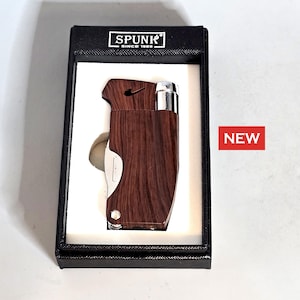 May include: A wood-effect lighter with a silver accent, presented in a black box. The lighter features a silver blade and a black logo. The box is labelled "SPUNK SINCE 1988". A red "NEW" sticker is on the right.