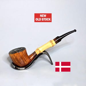 May include: A tobacco pipe with a wooden bowl and a bamboo stem, resting on a metal stand. The stem is light-colored bamboo with dark brown accents. The text "NEW OLD STOCK" is in a red rectangle.