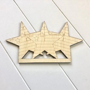 Puede incluir: Corte de madera de tres estrellas superpuestas en forma de corona. Las estrellas están decoradas con un patrón de rayas rojas, blancas y azules que recuerda a la bandera estadounidense.