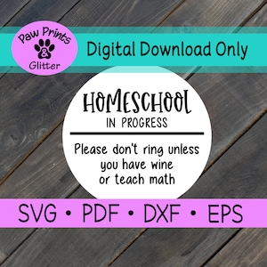 May include: A white circle with a blue border and black text that reads "HOMESCHOOL IN PROGRESS" and "Please don't ring unless you have wine or teach math". The circle is on a wood background with a pink and white circle that reads "Paw Prints & Glitter" in the top left corner. The text "Digital Download Only" is in blue text above the circle. The text "SVG PDF DXF EPS" is in black text below the circle.