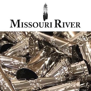 May include: A close-up shot of a pile of shiny, silver-colored metal objects. The objects appear to be decorative, with a detailed design. The text "MISSOURI RIVER" is displayed above the objects, along with a Native American feather symbol.