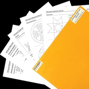 May include: A stack of white paper appliqué templates with black line drawings and text, including "Wheels & Arrows" and "Sioux Stars." An orange manila folder with a label that reads "Appliqué Template Pack #5" is in the foreground.