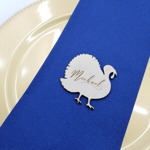 May include: A wooden turkey place card with the name "Michael" engraved on it. The place card is on a blue tablecloth.