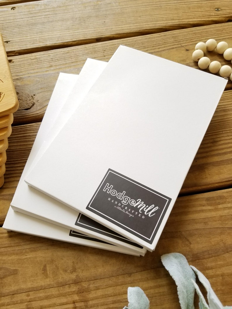 May include: Stack of three white blank canvases with a black and white logo that says "Hodgemill Handcrafted - little things"