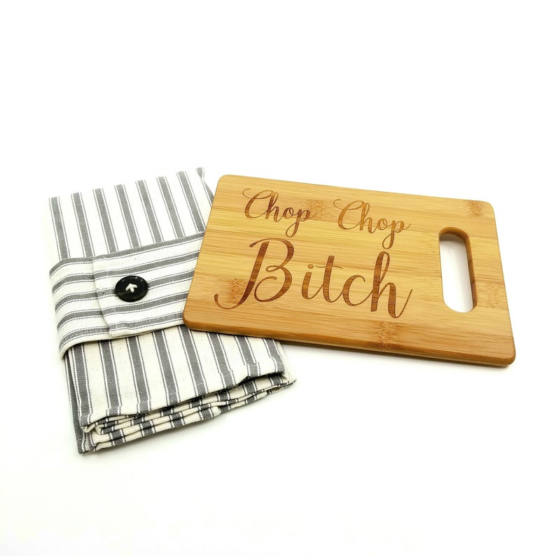 May include: A bamboo cutting board with a handle and the text "Chop Chop Bitch" engraved on it. The cutting board is paired with a striped kitchen towel.