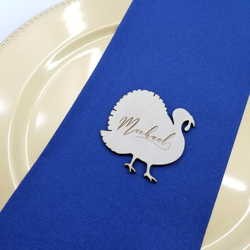 May include: A wooden turkey place card with the name "Michael" engraved on it. The place card is on a blue tablecloth.