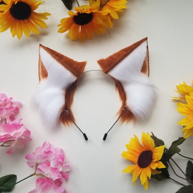 May include: A pair of brown and white furry cat ears headband. The headband is black and the ears are fluffy with white tips.