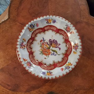 May include: A white metal serving tray with a red and gold border and a floral design. The flowers are in shades of pink, purple, yellow, and orange.