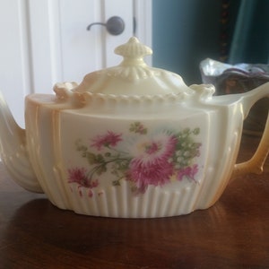 May include: A vintage porcelain teapot with a floral design. The teapot is white with gold accents and features a pink and white floral pattern.