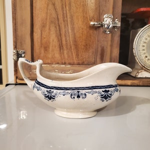 May include: A white ceramic gravy boat with a blue and white floral design. The boat has a handle on the left side and a spout on the right side.