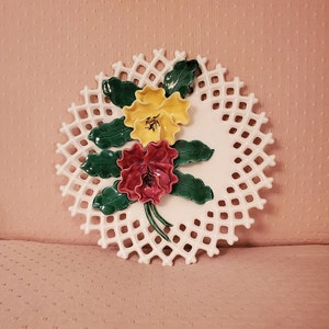 May include: A white ceramic plate with a lattice design and a raised floral motif. The flowers are yellow, red, and green.