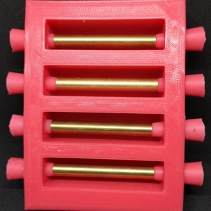 May include: A red plastic mold with five slots, each containing a gold metal rod. The mold is designed to hold and organize the rods.