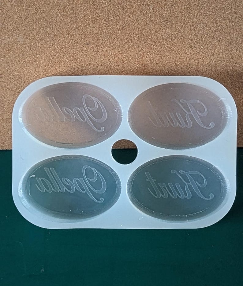 May include: A white silicone mold with four oval-shaped cavities. Each cavity has the word "Kurt" or "Opella" inscribed in a cursive font.