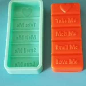 以下が含まれることがあります： 緑色のシリコンモールドと、各セクションに「Take Me」、「Melt Me」、「Smell Me」、「Love Me」のテキストが書かれた赤いチョコレートバーです。