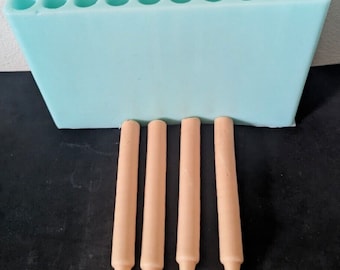 May include: A light blue silicone mold with ten round cavities for making candles. Four beige candles are sitting in front of the mold.
