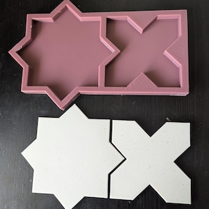 Puede incluir: Un molde de silicona de color malva con dos formas geométricas, una estrella de ocho puntas y una cruz. Debajo, cuatro baldosas blancas, dos en forma de estrella y dos en forma de cruz, probablemente hechas con el molde. Las baldosas tienen una textura moteada.