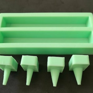 May include: A light green silicone soap mould with two rectangular cavities and four matching soap stamps. The soap mould and stamps are made of a flexible, food-grade silicone material.