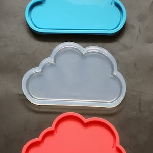 Puede incluir: Tres bandejas de silicona en forma de nube, una azul, una transparente y una roja.