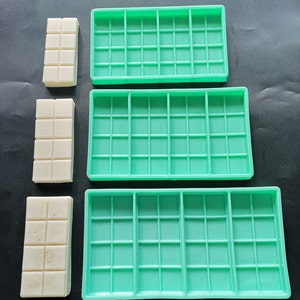 May include: Three green silicone molds for making rectangular bars of soap or wax. The molds are different sizes and have a grid pattern.