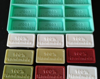 May include: A teal silicone soap mould with 12 rectangular cavities, each imprinted with the text "Noor ebembneH". Below are nine rectangular soaps in white, green, and red, each stamped with "100% Handmade".