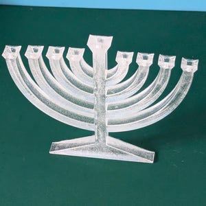 Może przedstawiać: Srebrny świecznik chanukowy z dziewięcioma miejscami na świece. Świecznik ma centralny trzon i zakrzywione ramiona.