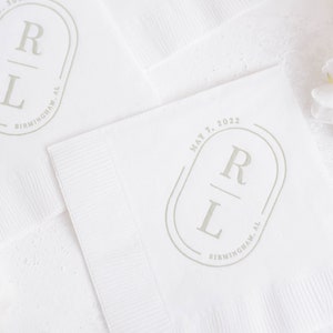 May include: White paper napkins with a gray oval monogram design featuring the letters "R" and "L" with the text "BIRMINGHAM, AL" and the date "MAY 7, 2022".