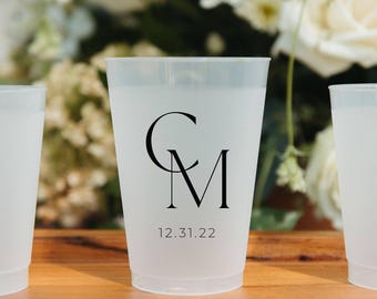 May include: A frosted translucent plastic cup featuring a black printed monogram with the letters CM and the date 12.31.22 below it. The cup has a tapered cylindrical shape with a smooth rim and a flat base, designed for holding beverages.
