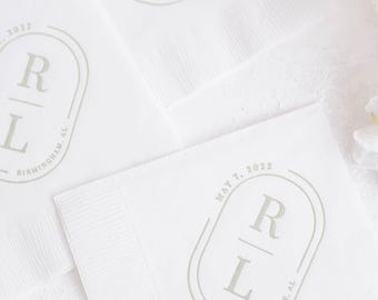 May include: White paper napkins featuring a gray oval emblem with the letters R and L stacked vertically. The text May 7, 2022 is printed along the top curve of the oval, and Birmingham, AL is printed along the bottom curve of the oval design.