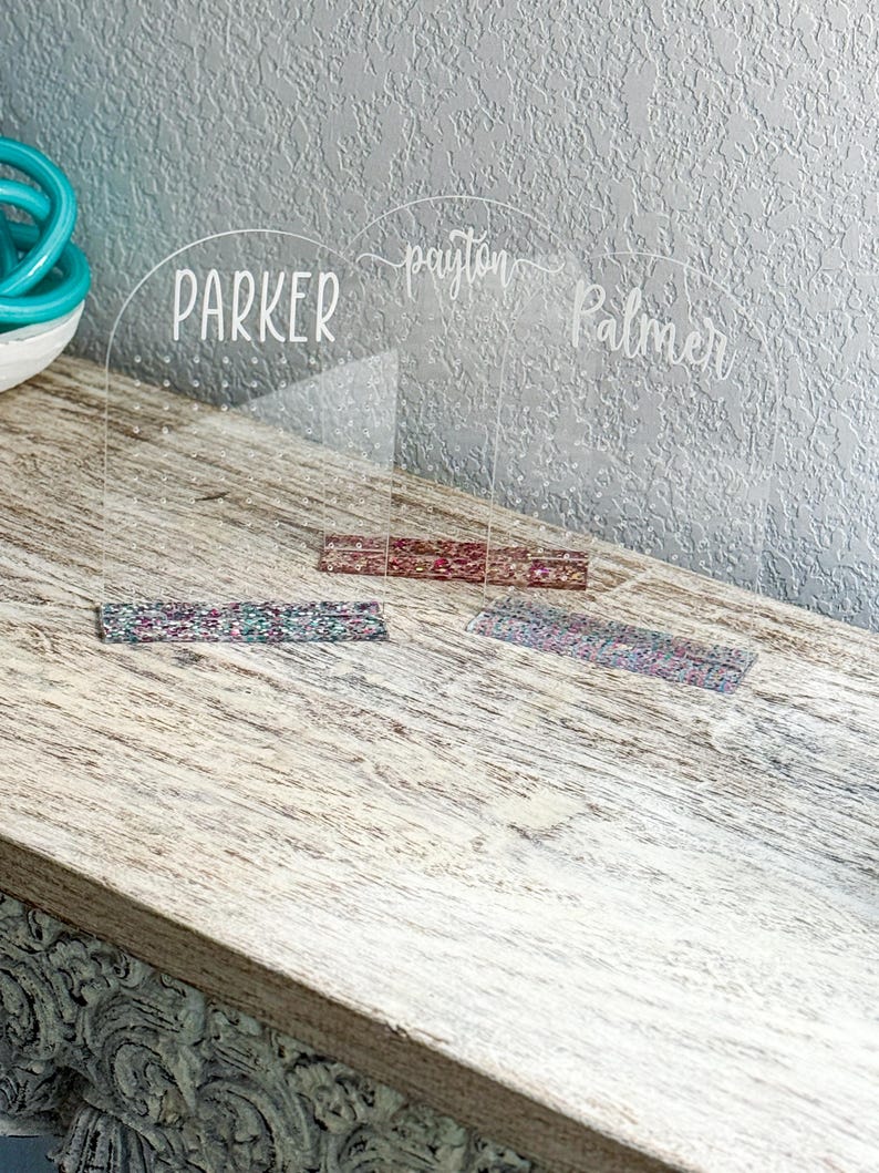 May include: Two clear acrylic earring holders with the names "Parker", "Payton Palmer" written on them. Each holder has a row of holes for earrings and a decorative strip of fabric at the bottom.