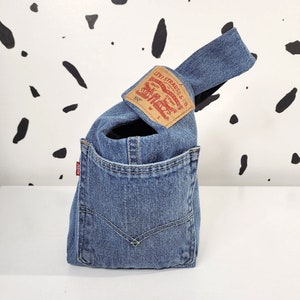 May include: A blue denim tote bag with a brown leather handle and a Levi's patch on the front. The patch has the text "Levi Strauss & Co." and "501" in red.