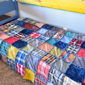 May include: A colourful patchwork quilt, featuring red, blue, yellow, and green squares, covers a blue bed frame. The quilt's squares are sewn together, creating a textured, cosy look. The bed frame is also painted blue, adding to the overall aesthetic.