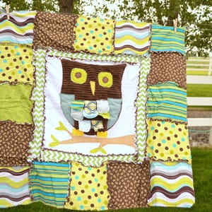 May include: A handmade patchwork quilt featuring a central owl design. The quilt showcases a variety of fabrics in shades of brown, green, yellow, and blue. The owl is brown with yellow eyes and is perched on a branch.