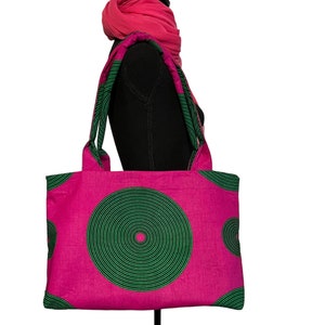 May include: A pink tote bag with green concentric circle designs. The bag has two long handles.
