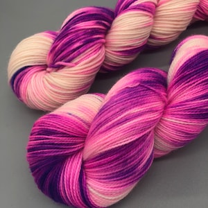 May include: A skein of yarn with pink, white, and purple stripes. The yarn is soft and fluffy, and it would be perfect for knitting or crocheting.